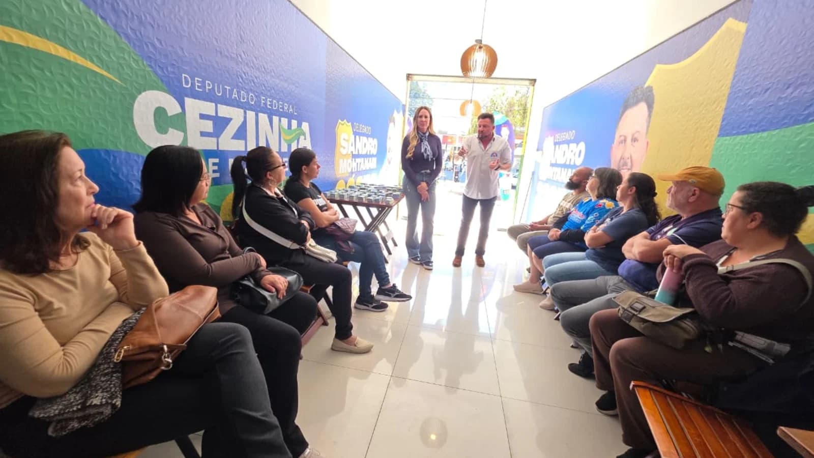 Sandro e vereadora Fabiana estão em pé e conversam com pessoas sentadas