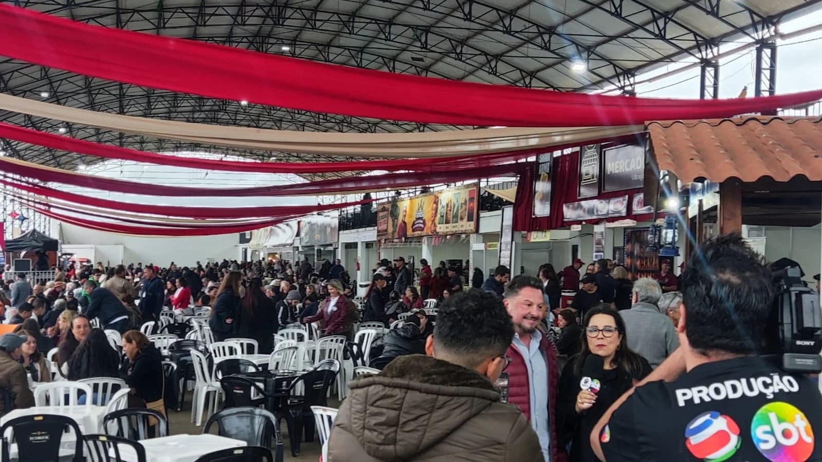 Delegado Sandro sendo entrevistado pelo SBT e participantes da Festa da Linguiça ao fundo